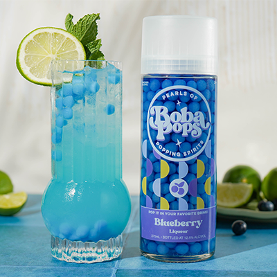 Blue cocktail with lime garnish next to a bottle of Boba POPS Blueberry liqueur.