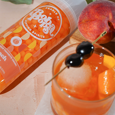Bottle of Boba POPS peach-flavored spirit with a cocktail garnished with cherries and an apricot.