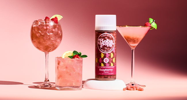 Bottle of Boba POPS Raspberry flavor with three pink cocktails on a pink background