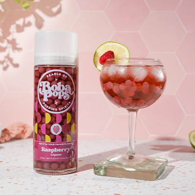 Baba POPS raspberry liqueur bottle with a glass of raspberry cocktail on a pink background